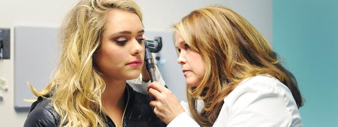 Health practitioner looking in student's ear with otoscope